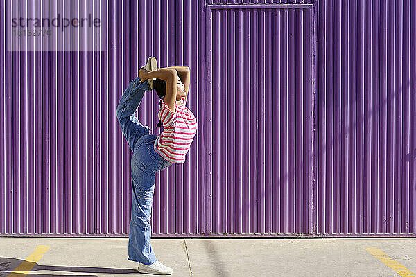 Young woman doing stretching exercise in front of corrugated wall