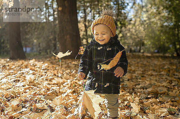 Lächelnder Junge mit Strickmütze spielt im Herbst im Park