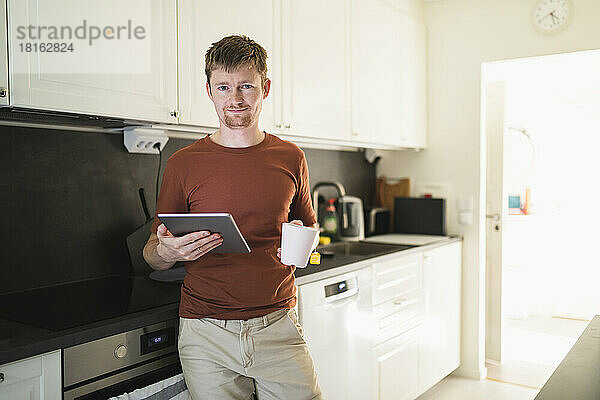 Mann mit Tisch-PC und Kaffeetasse in der heimischen Küche