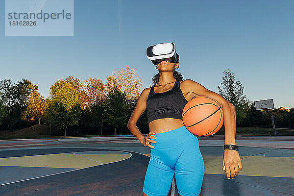 Junger Basketballspieler mit Ball und VR-Brille bei Sonnenuntergang