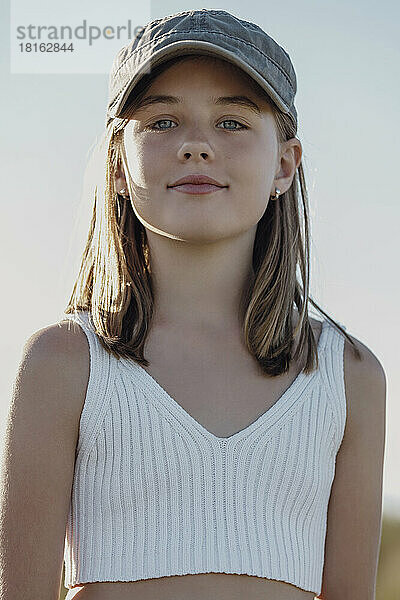 Lächelndes süßes Mädchen mit Mütze an sonnigem Tag
