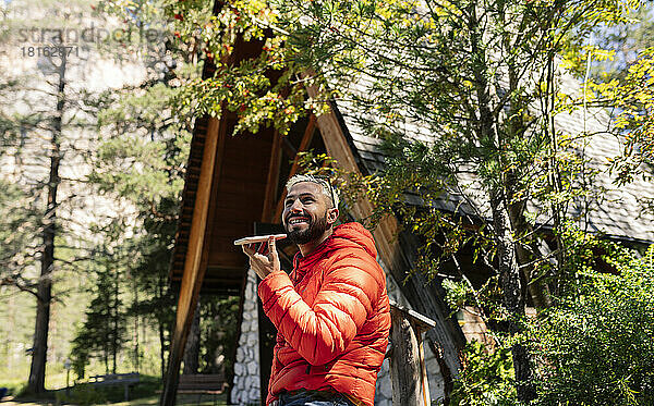 Glücklicher Mann  der vor der Hütte steht und mit seinem Smartphone spricht