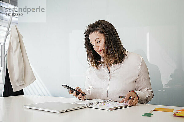 Reife Geschäftsfrau benutzt Smartphone am Schreibtisch im Büro