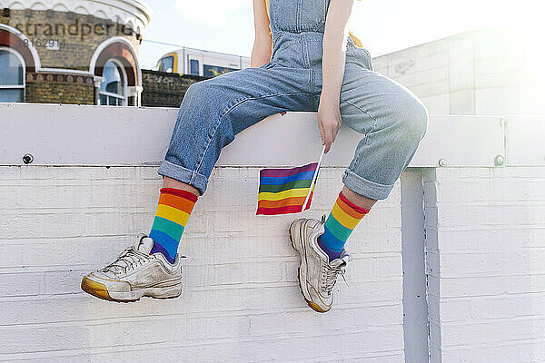 Transgender-Person mit Regenbogenfahne sitzt an der Wand