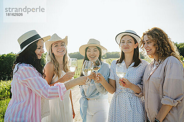 Fröhliche Frauen genießen an einem sonnigen Tag das Weinanstoßen im Weingut