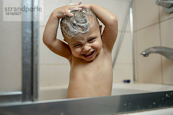Happy baby boy washing hair in bathtub