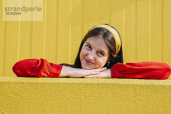 Lächelnde schöne Frau  die sich an die gelbe Wand lehnt
