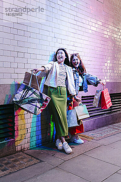 Fröhliches lesbisches Paar mit Einkaufstüten an einer Ziegelwand