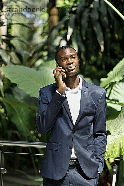 Businessman talking on smart phone in front of plants