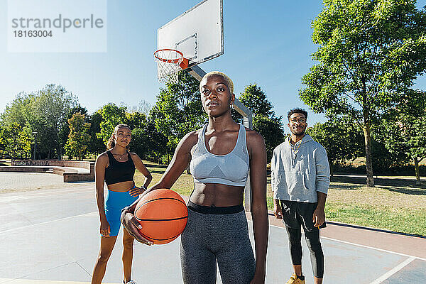 Selbstbewusste Freunde mit Ball auf dem Basketballplatz an einem sonnigen Tag