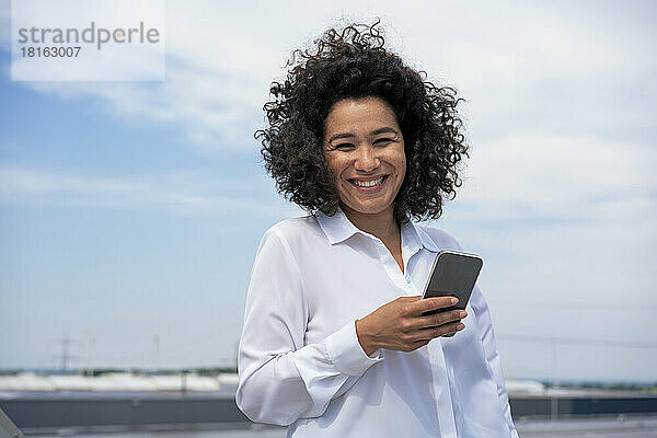 Glückliche Geschäftsfrau hält an einem sonnigen Tag ihr Mobiltelefon in der Hand