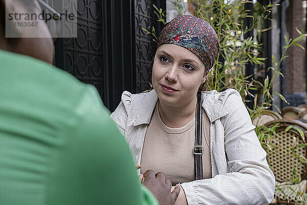 Junge Frau mit Kopftuch unterhält sich mit Freundin im Straßencafé