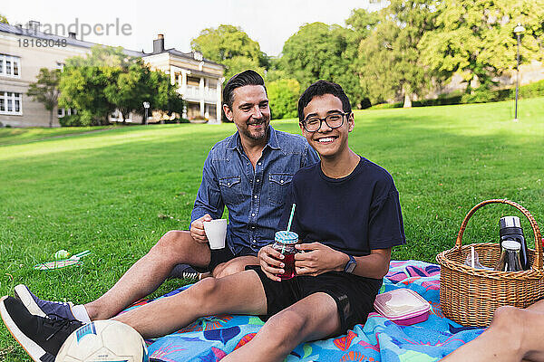 Glücklicher Junge genießt Picknick mit Vater  der im Rasen sitzt