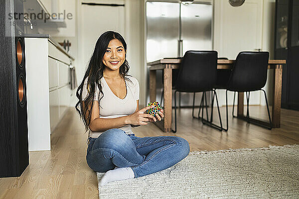 Glückliche Frau mit Puzzlewürfel  die zu Hause auf dem Teppich sitzt