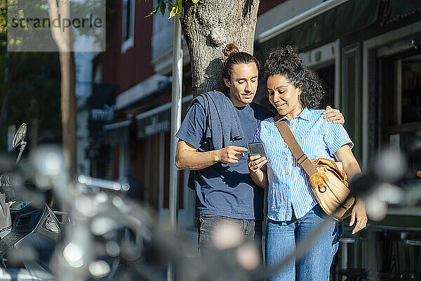 Frau teilt Mobiltelefon mit Freund am Baumstamm