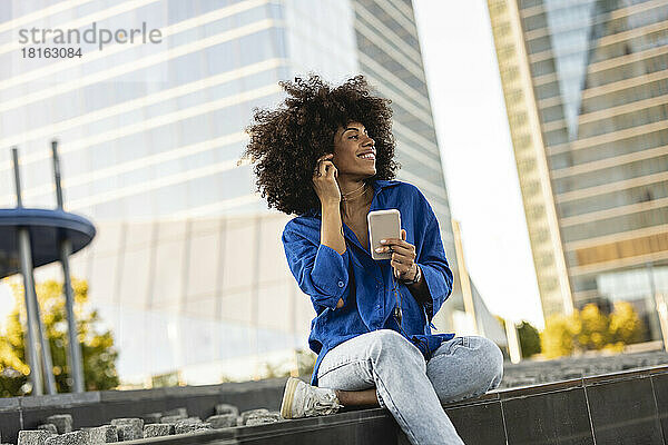 Glückliche Afro-Frau mit Mobiltelefon sitzt an der Wand