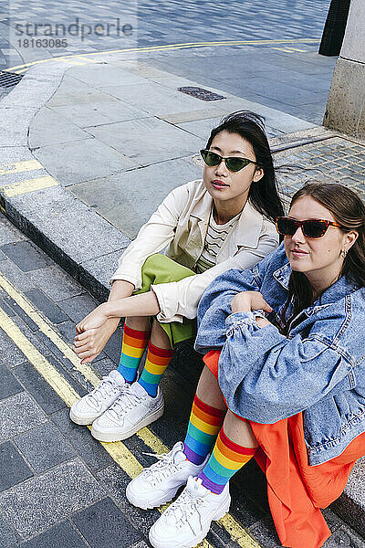 Junges schwules Paar mit Sonnenbrille sitzt auf Fußweg
