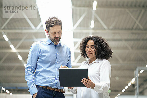 Lächelnde Geschäftsfrau diskutiert mit Kollegen über Tablet-Computer