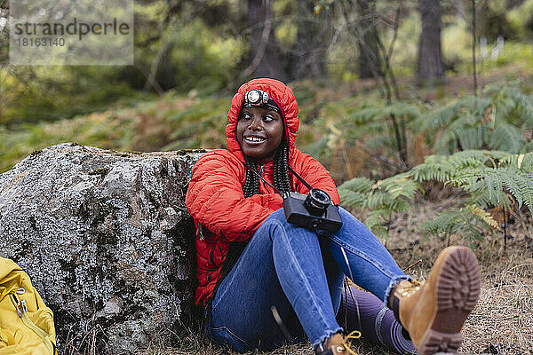Lächelnde Frau mit Taschenlampe sitzt mit Kamera im Wald