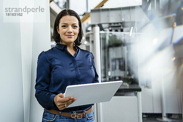 Lächelnde Geschäftsfrau hält Tablet-PC an der Wand in der Industrie