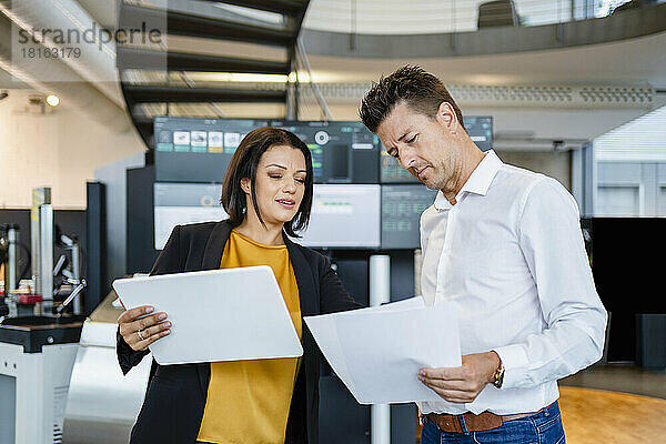 Geschäftsfrau hält Tablet-PC in der Hand und prüft Papier  während sie einem Kollegen in der Industrie zur Seite steht