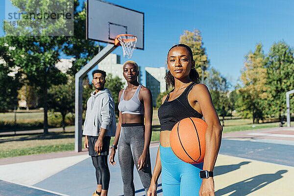 Junger selbstbewusster Basketballspieler mit Sportball von Freunden vor Gericht