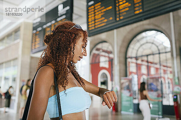 Junge Frau überprüft die Zeit auf einer Armbanduhr  die am Bahnhof steht
