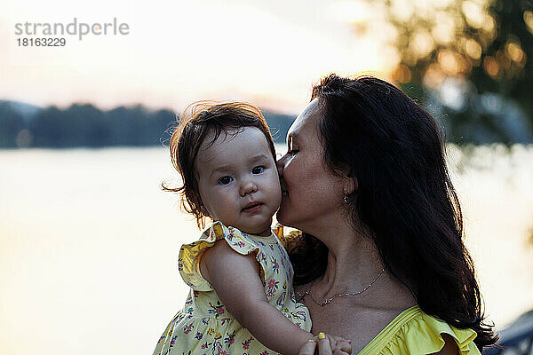 Mutter küsst Tochter bei Sonnenuntergang vor dem Fluss