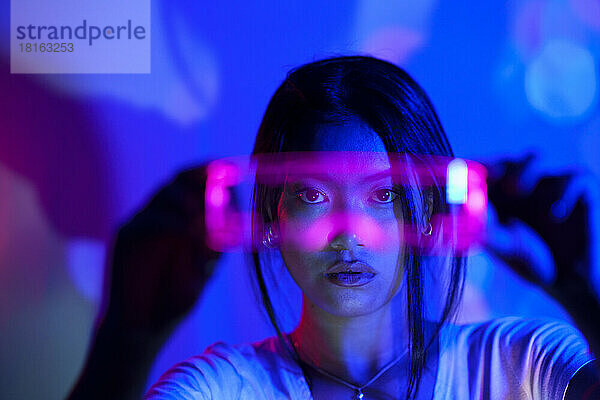 Junge Frau blickt durch eine futuristische LED-Brille