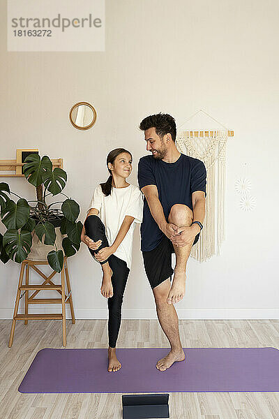 Lächelnder Mann mit Tochter beim Yoga auf der Gymnastikmatte zu Hause