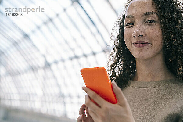 Lächelnde Frau mit Mobiltelefon am Bahnhof