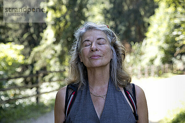 Ältere Frau mit geschlossenen Augen atmet frische Luft im Wald ein