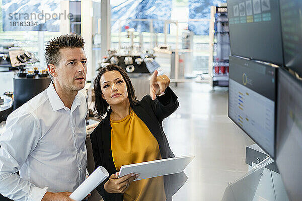 Geschäftsfrau hält Tablet-PC in der Hand und gestikuliert neben einem stehenden Geschäftsmann