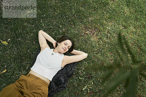 Woman with hands behind head relaxing on grass