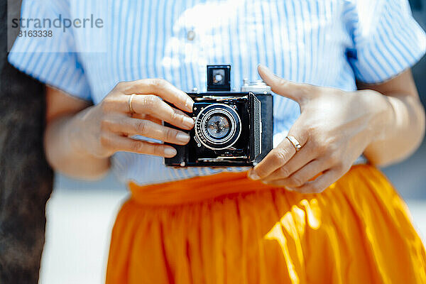 Frau hält an einem sonnigen Tag eine analoge Vintage-Kamera in der Hand