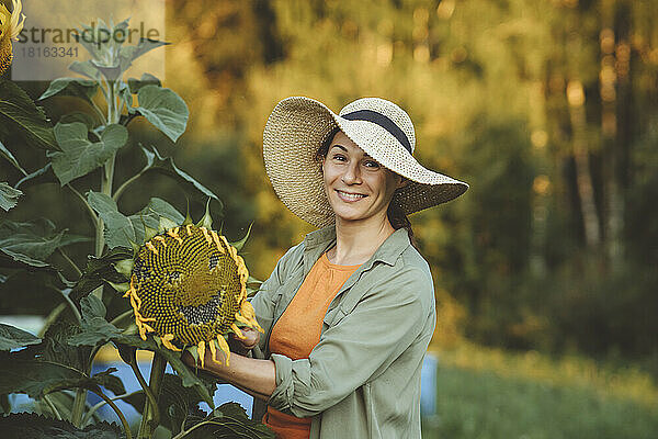 Lächelnde Frau hält Sonnenblume mit Smiley im Garten