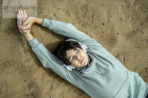 Junge trägt kabellose Kopfhörer und entspannt sich im Sand am Strand