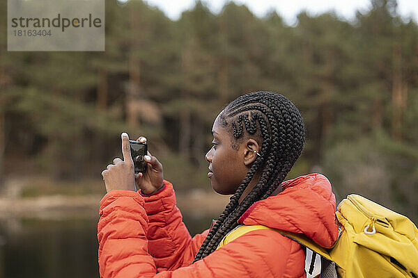 Junge Frau mit geflochtenem Haar fotografiert mit Smartphone
