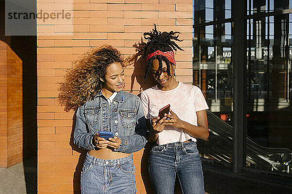 Junge Frau teilt an einem sonnigen Tag ihr Smartphone mit einer Freundin