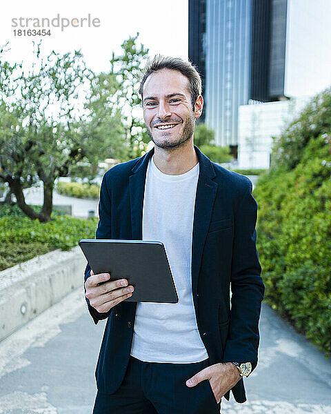 Glücklicher Geschäftsmann mit Tablet-PC  der im Büropark steht