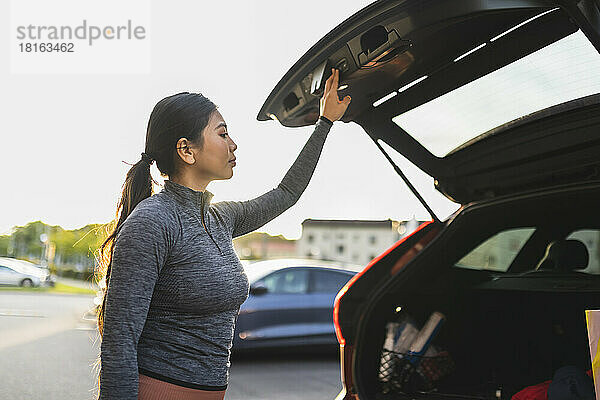 Junge Frau öffnet auf Roadtrip die Kofferraumtür eines Autos