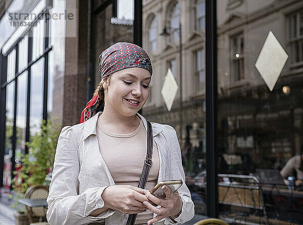 Glückliche Frau mit Bandana und Smartphone im Straßencafé