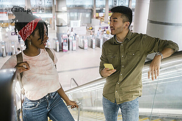 Junger Mann und Frau unterhalten sich auf der Rolltreppe am Bahnhof