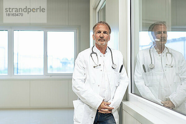 Oberarzt lehnt an Glasfenster