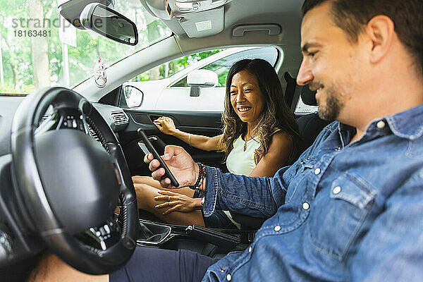 Smiling woman looking at man using smart phone sitting in car