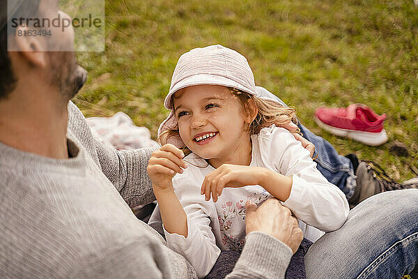 Smiling girl looking at father sitting on grass