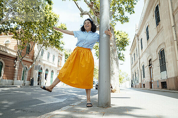 Verspielte Frau hält Pole Dance auf dem Bürgersteig in der Stadt