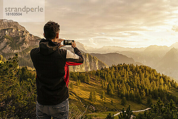 Mann fotografiert Berg mit Smartphone bei Sonnenuntergang