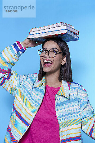 Glückliche Frau mit buntem Reißverschluss und Büchern auf dem Kopf vor blauem Hintergrund