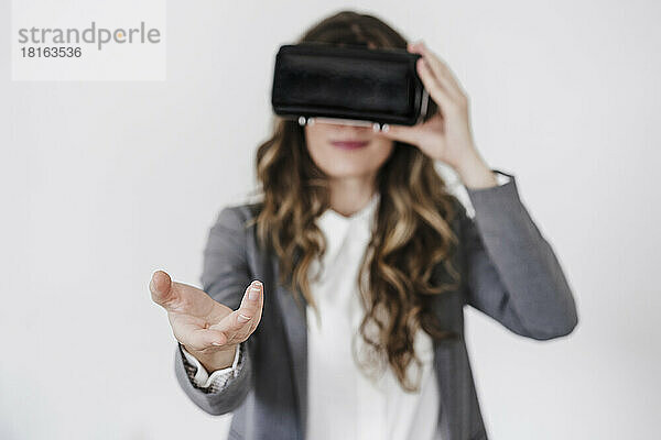 Gestikulierende junge Geschäftsfrau nutzt Virtual-Reality-Simultor im Büro